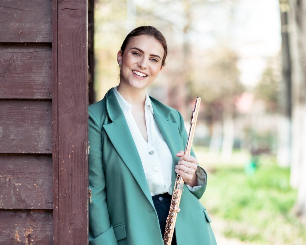 Musikerin sitzt mit einer Querflöte auf Steinstufen und blickt inspiriert in die Ferne – Symbol für Ruhe, Klarheit und Kreativität.